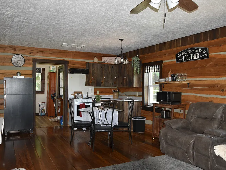 Charming rustic kitchen with warm wood-paneled walls, custom barn-wood cabinetry, and rich hardwood floors throughout. The open layout flows seamlessly into the dining and living areas, with full-size appliances and plenty of counter space!!