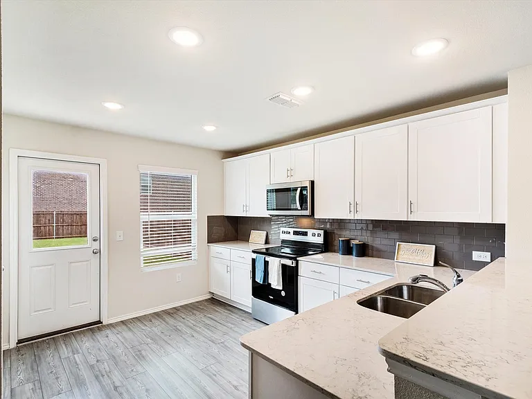 Contemporary kitchen featuring white shaker cabinetry, stainless steel appliances, light-toned countertops, and a subway tile backsplash