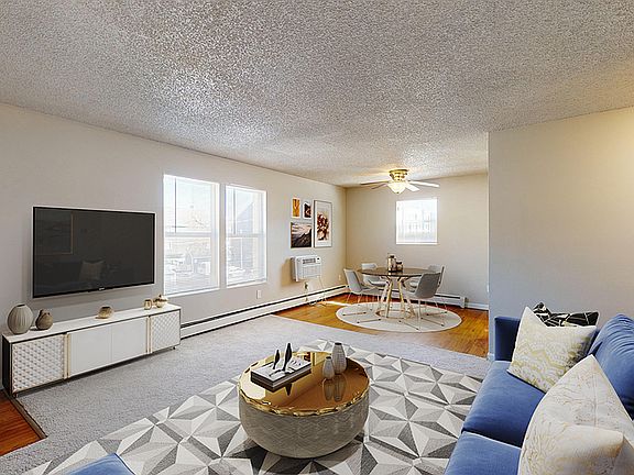 Inviting open-concept living room featuring a modern entertainment center, cozy blue sofa, and stylish dining area with ample natural light.