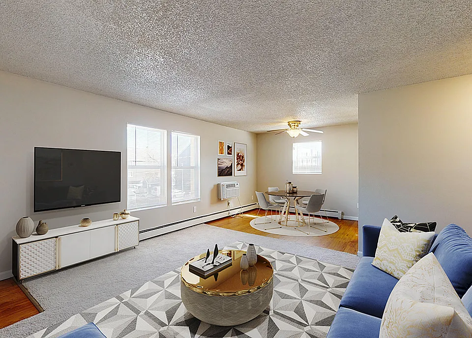 Inviting open-concept living room featuring a modern entertainment center, cozy blue sofa, and stylish dining area with ample natural light.