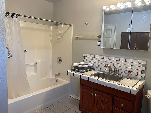 Bathroom with tiled flooring, full shower/bath, with tiled sink for washing dishes.
