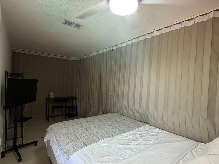 Private bedroom with a ceiling fan/light, tile flooring, and space for a bed plus a small TV or work setup.