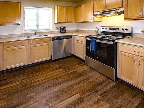 Chic kitchen with sleek stainless steel appliances, warm wooden cabinetry, and elegant countertops, complemented by rich hardwood floors.