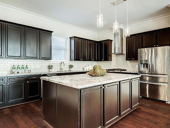 The spacious kitchen has tons of storage, ample cabinets, hanging pendant lighting and recessed lighting, wood floors, subway tiled backsplash and granite counters.
