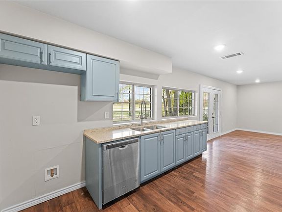 Kitchen featuring stainless steel dishwasher, light stone countertops, sink, and dark wood-type flooring