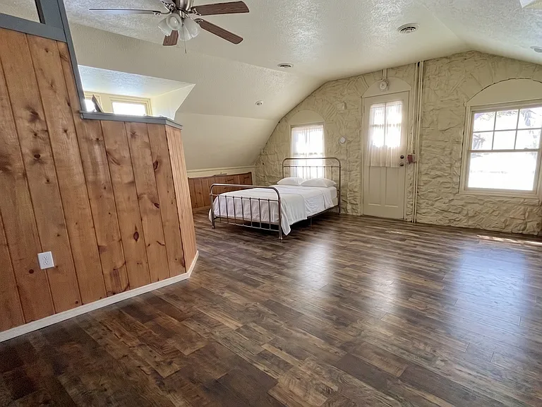 Expansive upper primary suite featuring unique stone architecture, a king bed, daybed, ample clothing storage, and a private balcony.