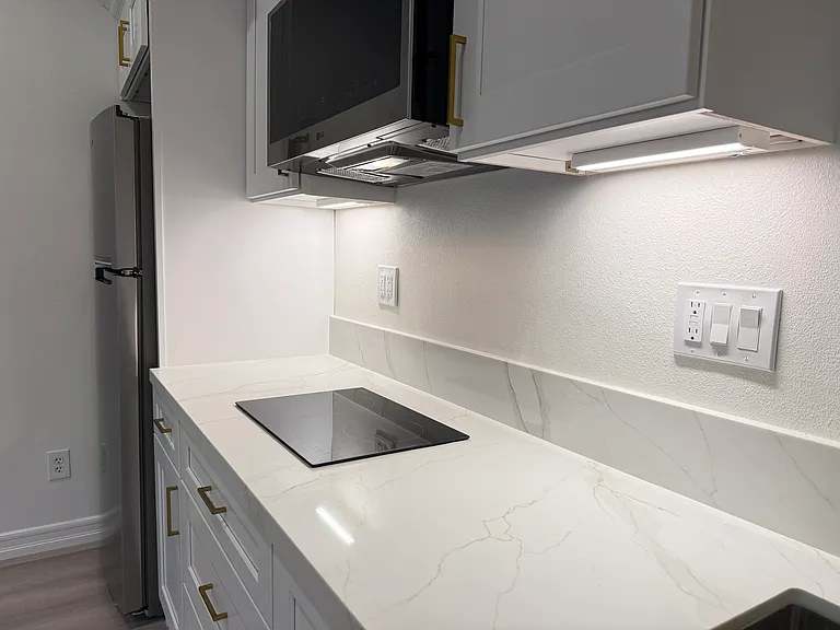 Modern kitchenette featuring quartz countertops, an LG microwave, under-cabinet lighting, and sleek contemporary finishes.