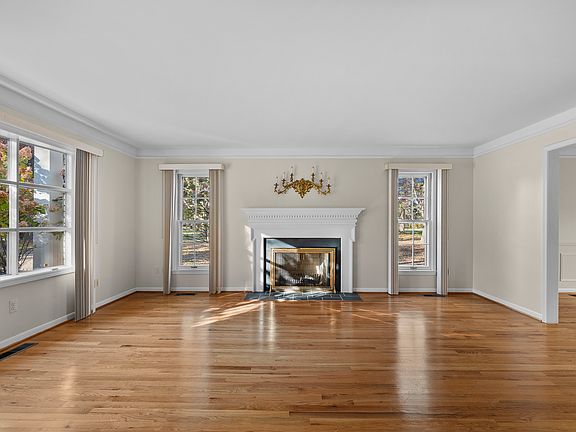 Bright living room with hardwood floors, picture windows, and fireplace centerpiece.