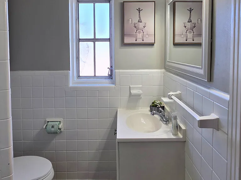 Bright clean bathroom with window, shower, sink, and wall art
