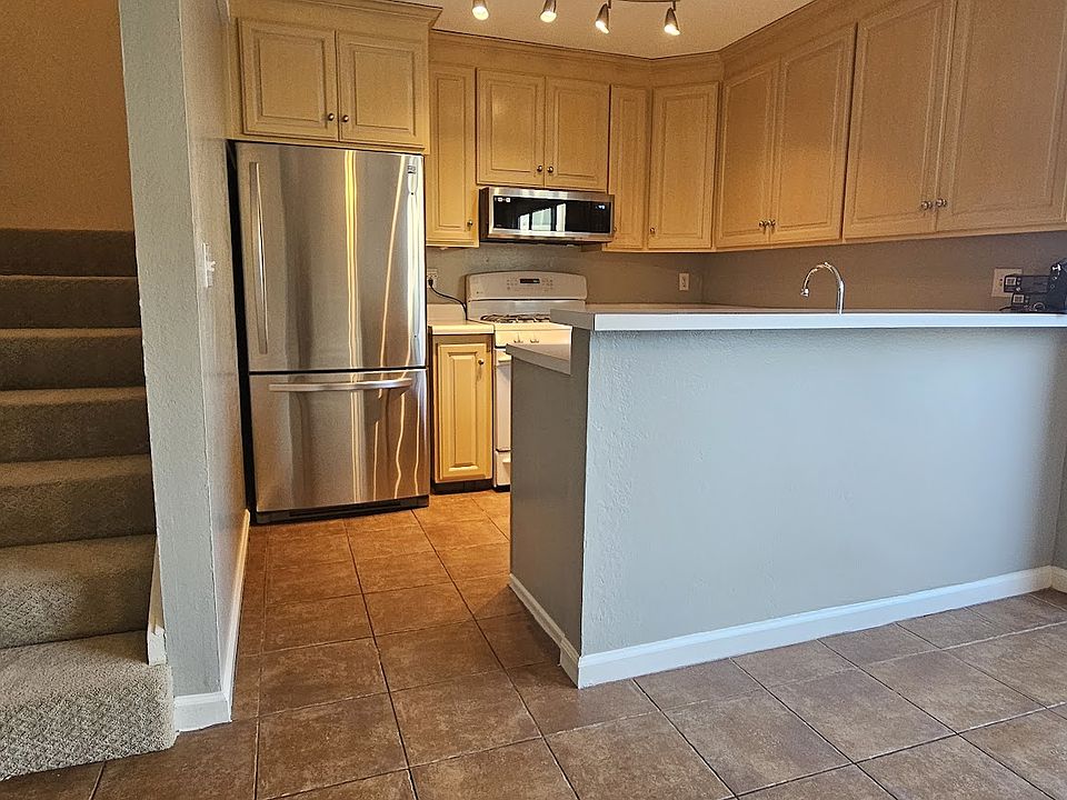 Open kitchen with stainless fridge, dishwasher, and microwave plus a white stove and ample cabinets. Breakfast bar opens to the living area. Bright sliding doors lead to a private patio, and a carpeted staircase brings you to the upper level.