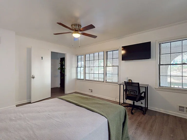 Spacious bedroom with large windows, ceiling fan, wall-mounted TV, and a dedicated desk area for work or study.