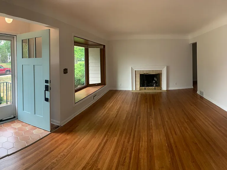 Living space with large bay window, wood burning fireplace and newly finished hardwood floors