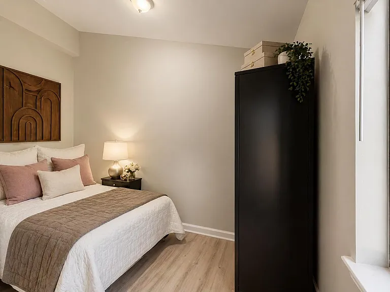 Well-appointed bedroom with a full bed, nightstand lighting, and a tall wardrobe for added storage near a large window.