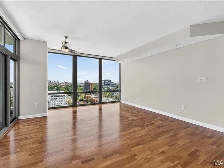 Spacious living area featuring expansive windows, wood-finish flooring, a contemporary ceiling fan, and a glass door leading to an outdoor balcony