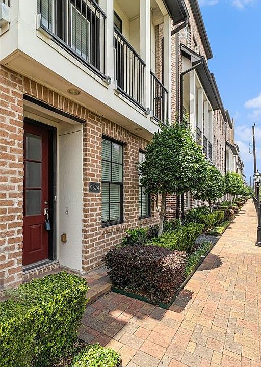 This is a welcoming entryway featuring a red door, surrounded by attractive exposed brickwork. The residence has well-maintained greenery by the door, adding to the home's curb a