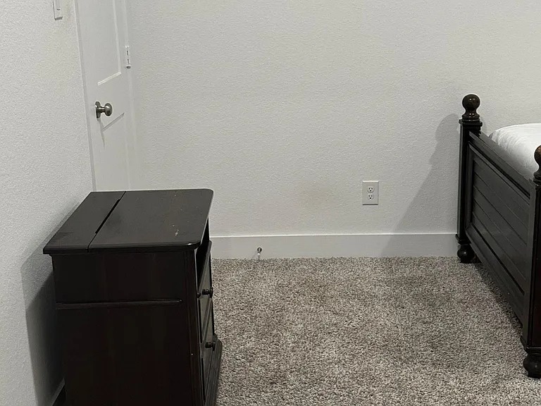 Carpeted bedroom with a classic bed frame and dresser, offering a simple layout with space for personal storage.