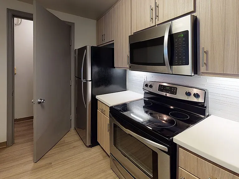 Apartment kitchen with wood floor, wood cabinets, and stainless steel appliances.