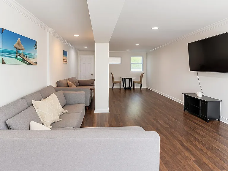 Open living area with sectional seating, wall-mounted TV, and a small dining nook, finished with hardwood-style floors.