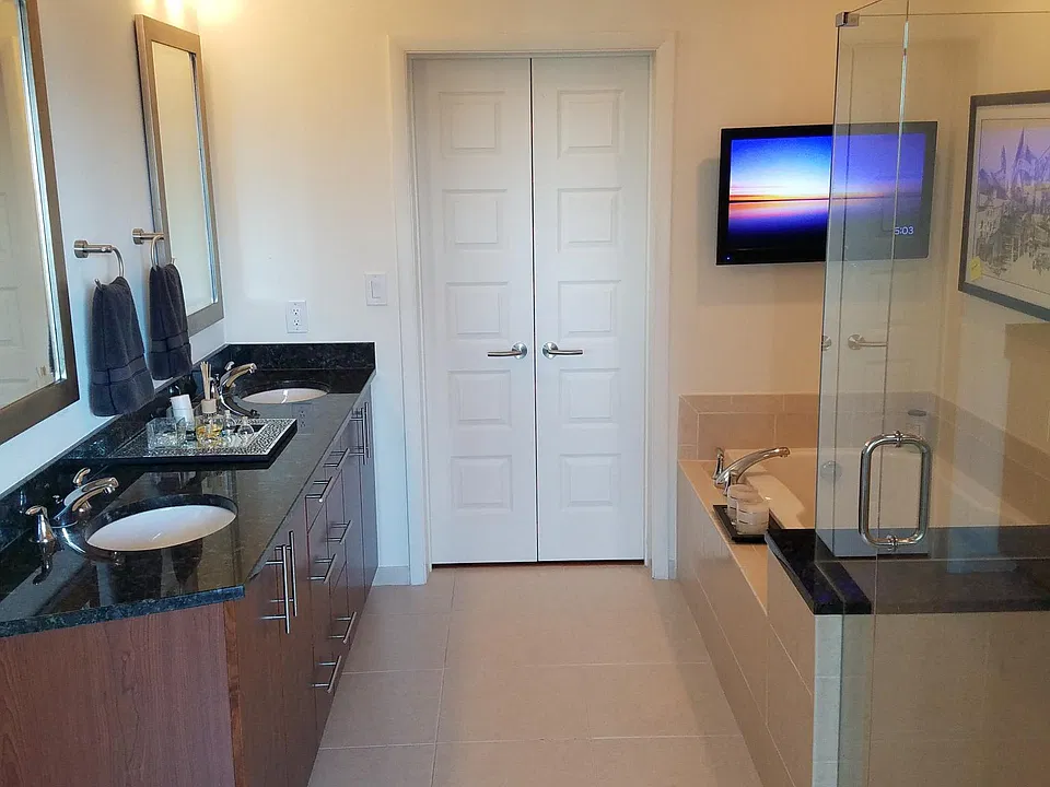 Master bathroom (as seen walking in from master bedroom) includes dual vanity sinks/mirrors, glass enclosed shower, large bath tub, and wall mounted tv and speakers. Mater walk-in closet is accessed through the master bathroom.