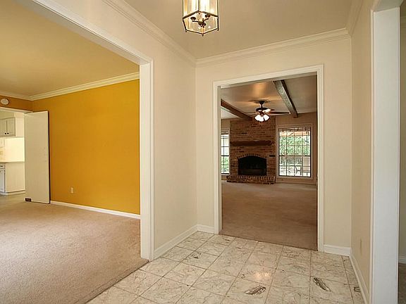 Straight ahead is the Family Room! You can already see the big ceiling beams. A brick fireplace with a sturdy mantel graces the fireplace. The original entry way tile is beautiful terrazzo. The carpet is neutral, clean and low.