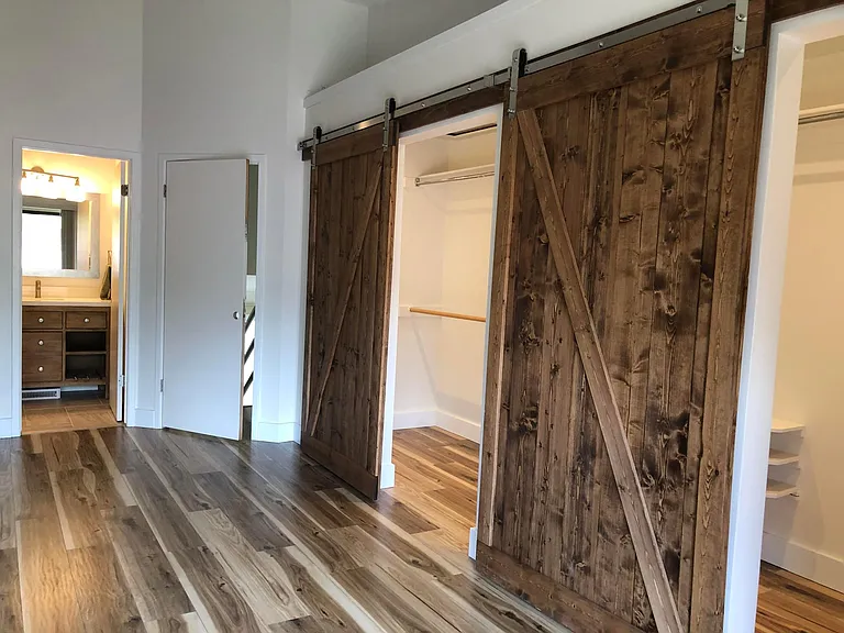 Beautiful sliding barn doors provide two wide access points to walk-in closet with motion sensing lighting. Entrance to Master Bath in the background.