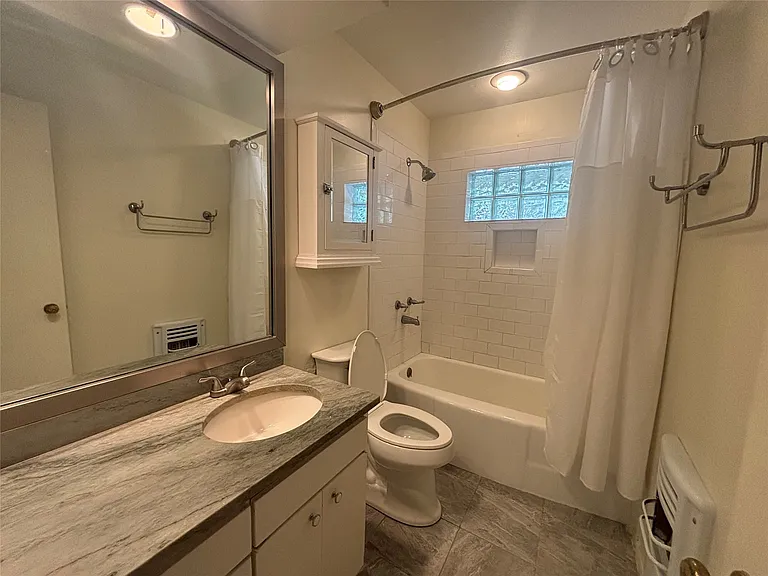 Bathroom featuring a vanity with an undermount sink and a patterned stone countertop, a large wall-mounted mirror, white subway tile shower surround with a built-in niche, glass block window, and a white medicine cabinet
