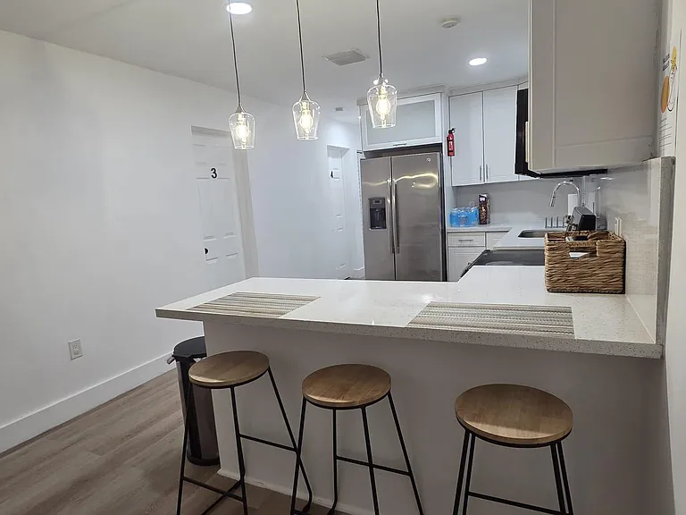 Kitchen with a long breakfast bar, pendant lighting, and stainless-steel refrigerator plus ample cabinetry and counter space.