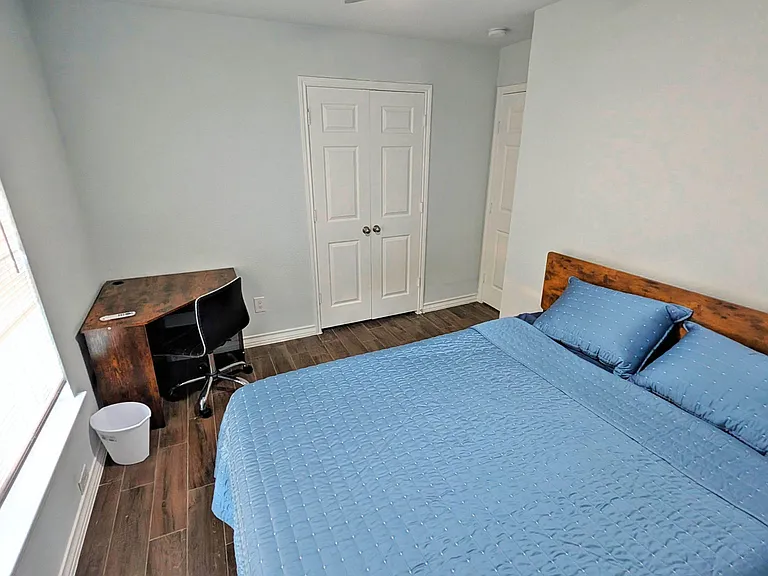 Private bedroom with a full bed, dedicated desk workspace, and double-door closet plus window blinds for light control.