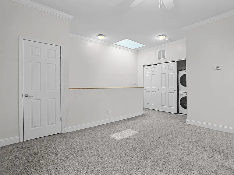Spacious second-floor bedroom with 10-foot ceilings, two windows with 2-inch wood Venetian blinds, soft carpeting, crown molding, a ceiling fan, and an included washer and dryer in the closet.