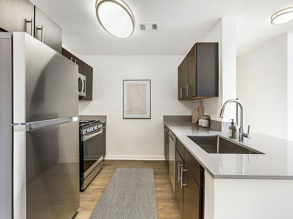Renovated Package I kitchen with stainless steel appliances, grey quartz countertops, dark brown cabinetry, white tile backsplash, and hard surface flooring