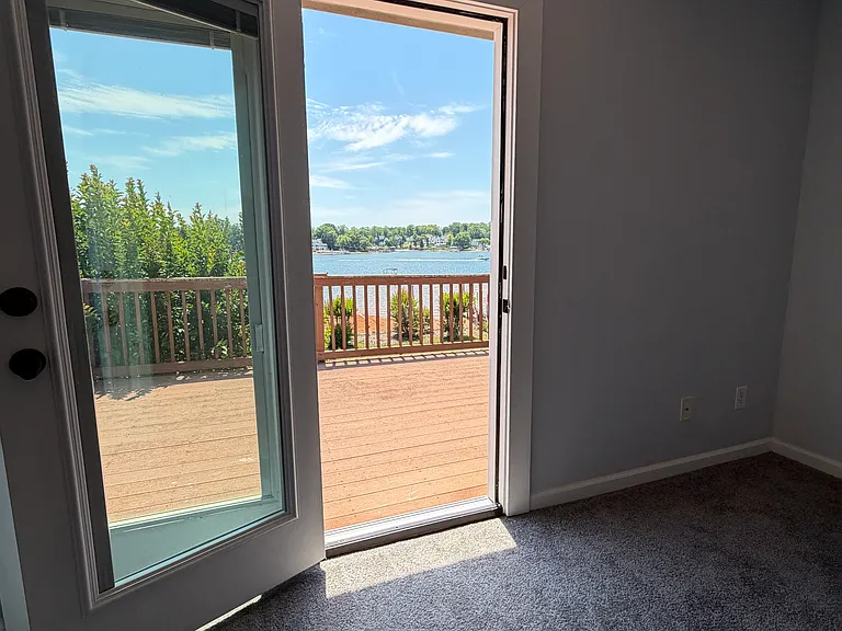 Every corner of this second-floor primary suite frames the lake_French doors swing open to a sprawling private deck, and even from the bedroom, unobstructed water views wrap around you.