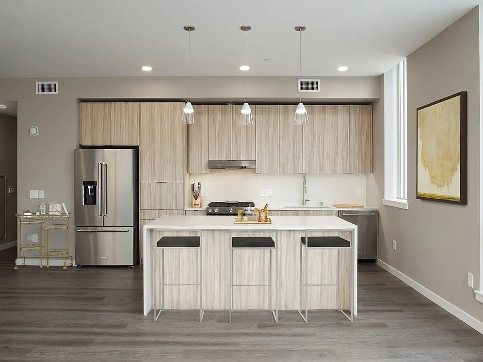 Signature Collection penthouse kitchen with oak cabinetry and undercabinet lighting, white quartz countertops and backsplash, upgraded stainless steel appliances, and hard surface flooring. - Avalon Belltown Towers