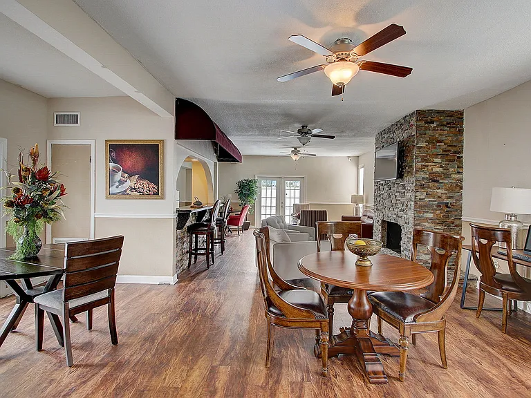 Inviting open-concept living space with elegant wooden flooring, cozy seating by a stone fireplace, and stylish dining area, perfect for entertaining.