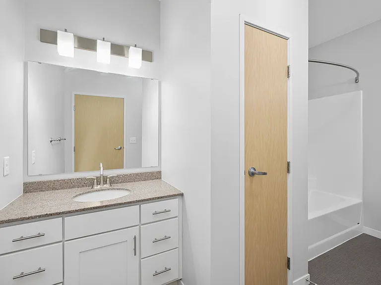 Chic and modern bathroom featuring sleek white cabinetry, a spacious vanity with granite countertop, and a well-lit mirror. Chic and modern bathroom featuring sleek white cabinetry, a spacious vanity with granite countertop, and a well-lit mirror.