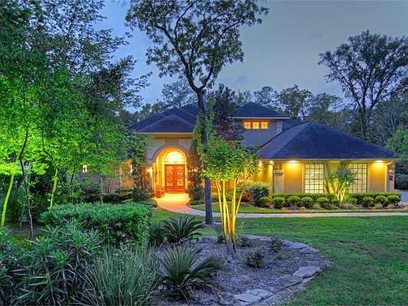 Front yard features lush landscaping, lighting, stacked stone, trees & rocks.