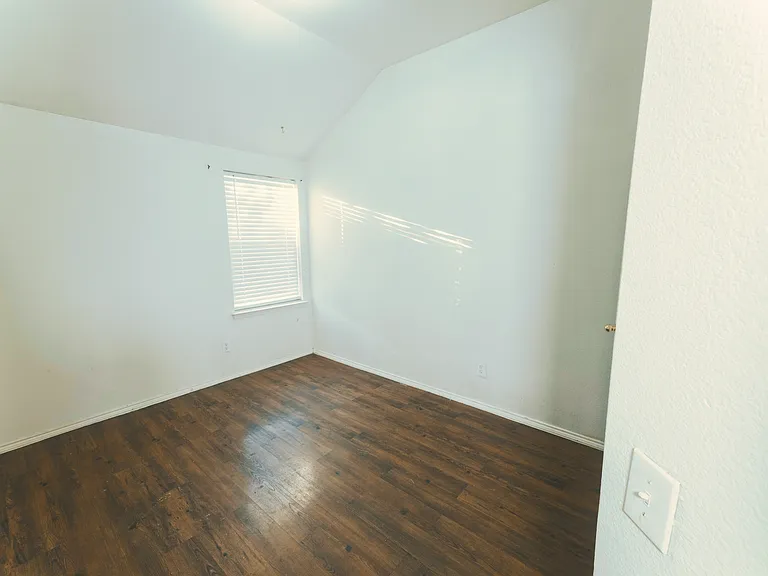 A bright and airy third bedroom with closet, featuring high vaulted ceilings and beautiful wood-style flooring that catches the afternoon sun