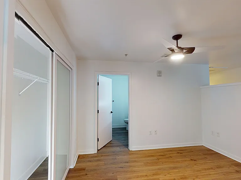 Spacious apartment bedroom with large closet, attached bathroom and wood-style flooring.