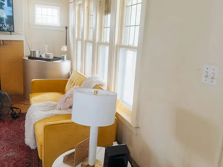Sunlit sitting area with large windows, a comfortable sofa, and side tablesideal for relaxing or reading.