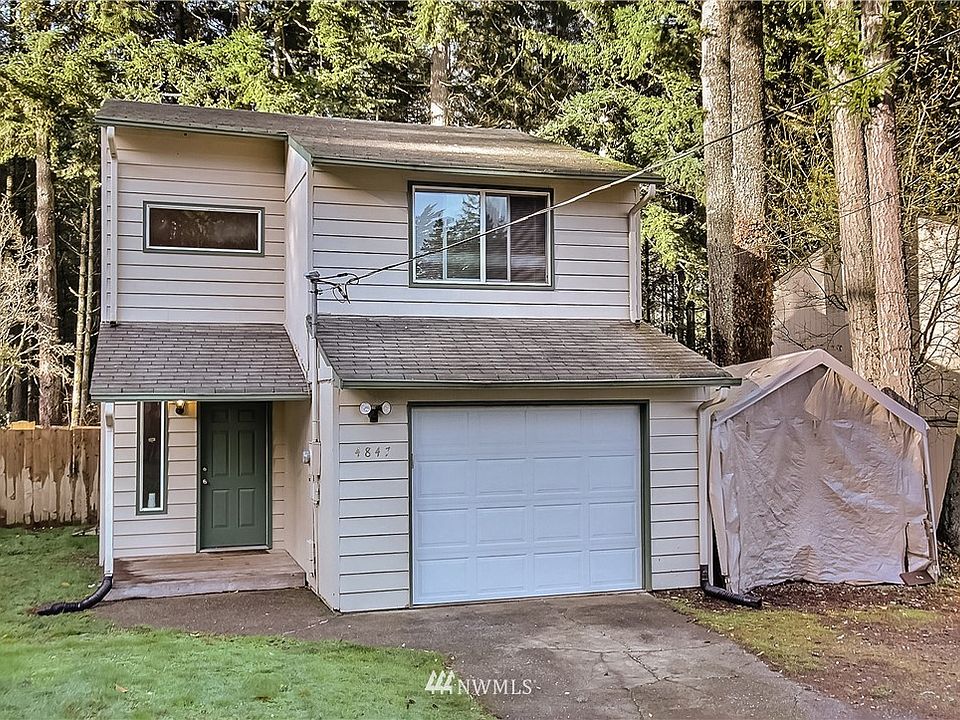 Front view of home, note all the woods behind the property and the tall trees! Carport to the right of garage is included :). 