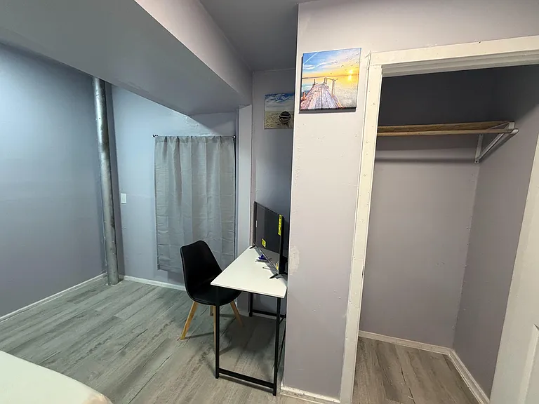 Bedroom with desk workspace and open closet area, finished with wood-look flooring and neutral walls.