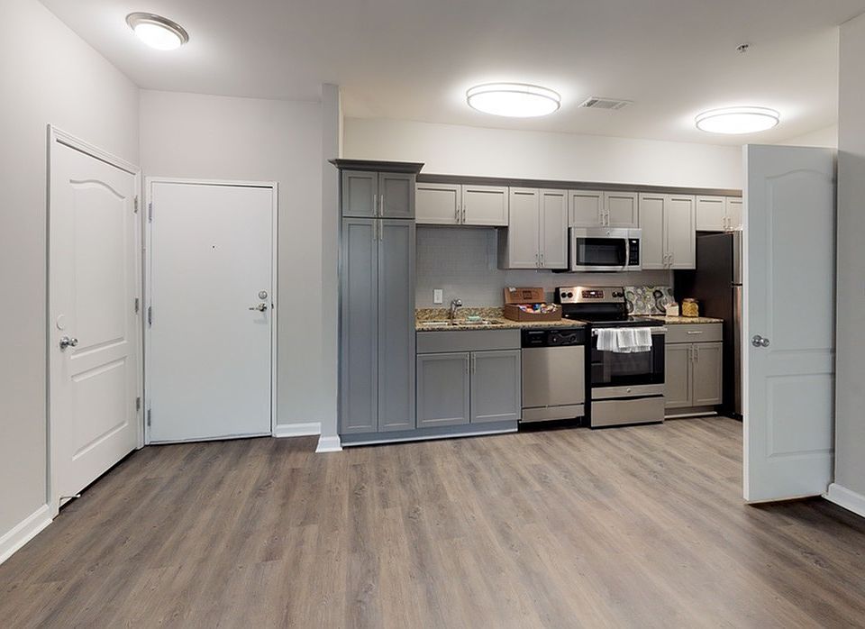 View from living room into kitchen with wood inspired vinyl plank flooring, shaker style cabinets with designer pulls and stainless steel appliances