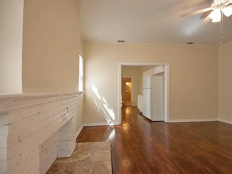 A spacious living room featuring hardwood floors, a fireplace and a ceiling fan, creating a bright and airy atmosphere.