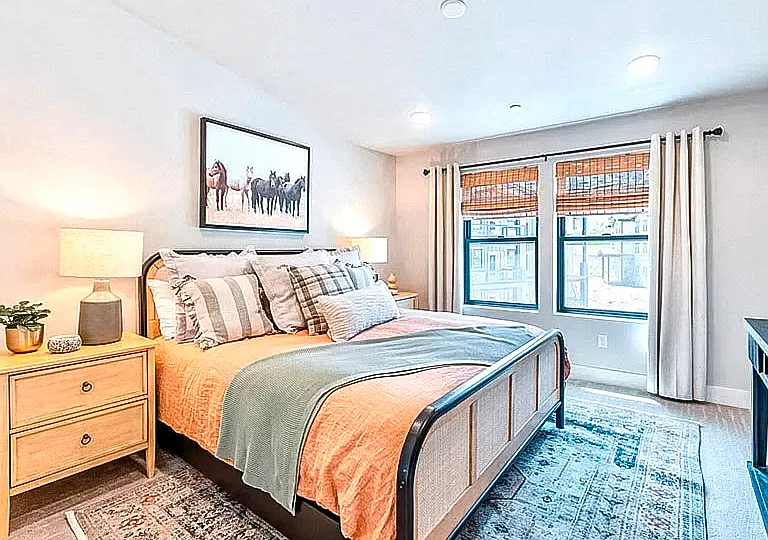 Spacious master bedroom with cozy bedding, wall art, bamboo blinds, and abundant natural light