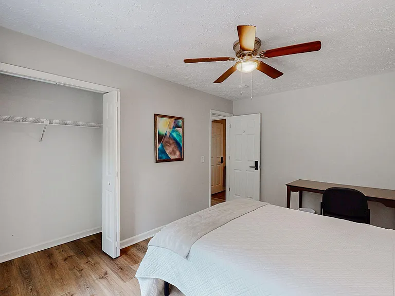 Bedroom includes a ceiling fan with light, closet with shelving, and space for a bed plus a small desk setup.