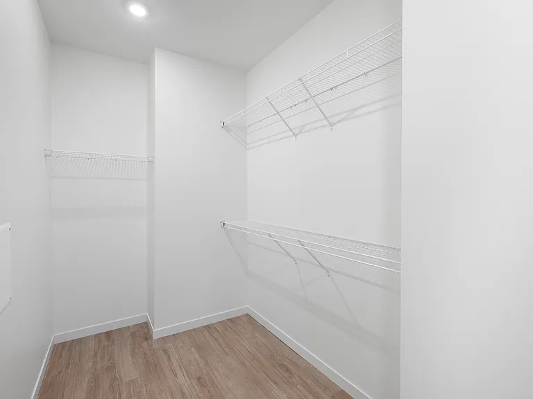 Bright, spacious walk-in closet with modern shelving and wood flooring, ideal for organized living. Bright, spacious walk-in closet with modern shelving and wood flooring, ideal for organized living.