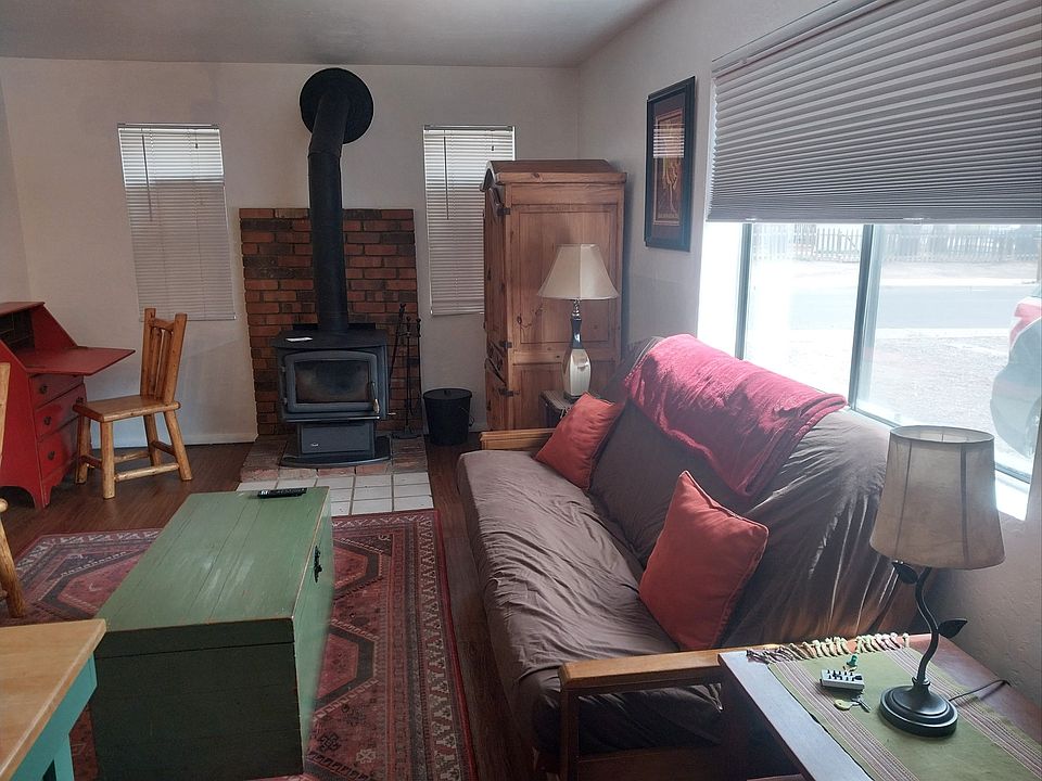 Open concept living/dining room with flat-screen TV, work area with desk and wood stove (not the only heat source)