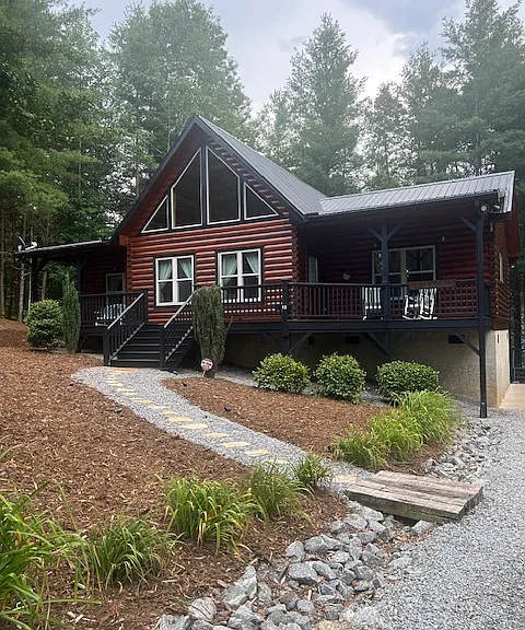 Newly painted inside and out cabin has a long gravel driveway and a cement area with a basketball hoop. Those are all lilies that bloom bordering the driveway.