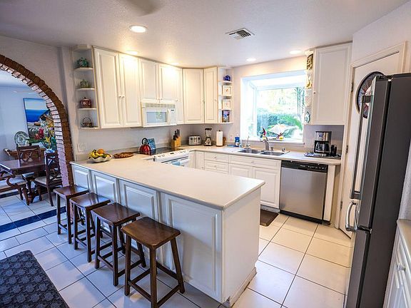 Main house kitchen with electric stove, microwave, dishwasher, refrigerator, double sink, bay window, ceiling fan.