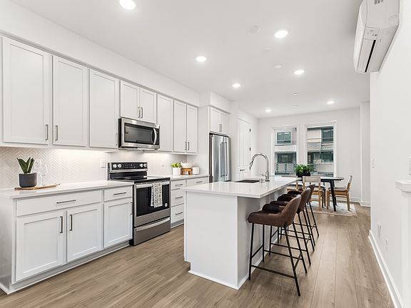 A modern, bright, and spacious kitchen with white cabinets, stainless steel appliances, and a wooden