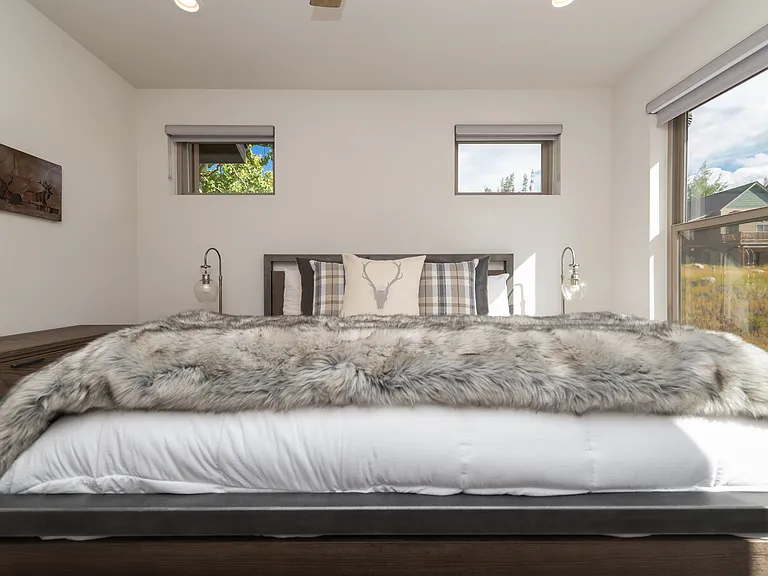 Bright and inviting primary suite on upper level with large windows, soft natural light, and luxurious mountain-inspired bedding for a restful retreat.